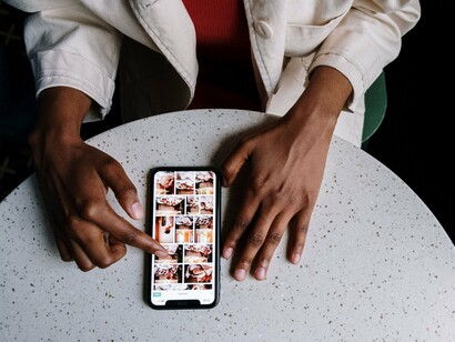 Vista de cima, uma pessoa navega pelo smartphone enquanto permanece à mesa. A conexão digital acompanha momentos banais da rotina e transforma hábitos cotidianos em informações valiosas para os sistemas que nos observam