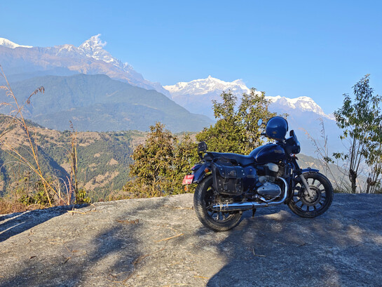 A solitary motorcycle rests quietly before the lush, rolling green mountains of Nepal’s Himalayan landscape
