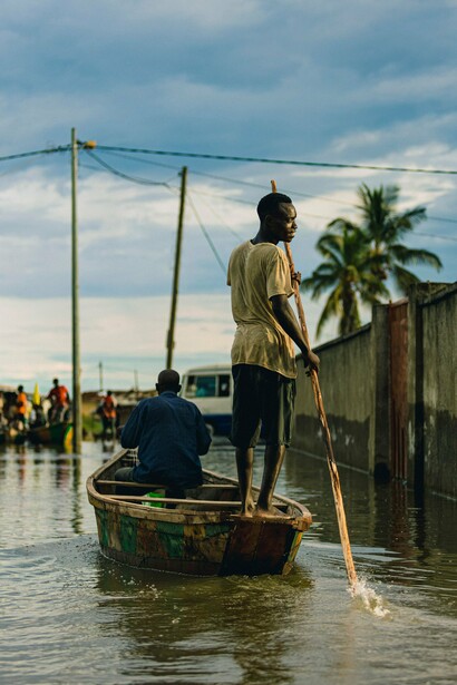 A resident steering a wooden boat through floodwaters, representing the daily reality of communities adapting to increasingly severe flooding