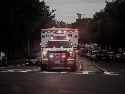 Amid daylight, a white and red ambulance truck speeds with sirens along the road