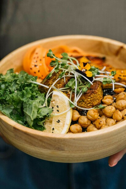Person holding a brown wooden bowl with an anti-inflammatory, balanced meal