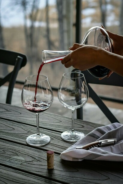 A person pouring Tazzelenghe wine from a decanter into a glass