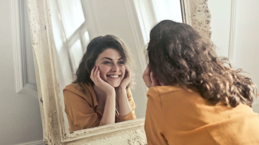 A woman smiling at herself in the mirror, smiling is a cause of happiness in your life