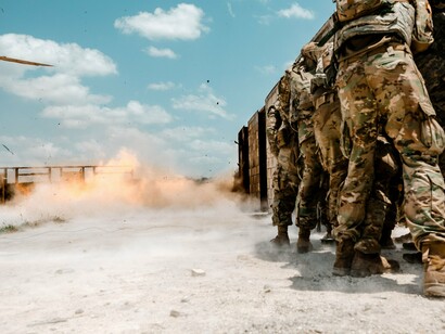 Soldados em uniformes camuflados se protegem diante de uma explosão durante um exercício militar. O treinamento reproduz situações de perigo para preparar tropas para um cenário que, na realidade, pode significar destruição e perda de vidas
