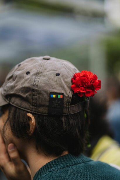 Jovem com uma rosa presa ao boné observa o ambiente à sua frente. O artigo aborda os desafios enfrentados por quem procura construir o futuro em um contexto de crescente incerteza social e económica