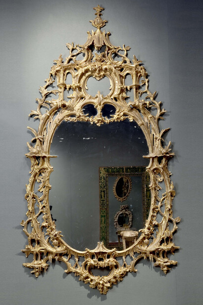 An exceptional English rococo carved and gilded mirror frame in the style of Thomas Johnson, the inner frame in the form of a cabochon created of double c-scrolls flanked by pagodas on either side and a pagoda at the base, the outer frame consisting of trailing vines and c-scrolls with rocaille.  Antique (18th Century) oval plate, not original.  English, Circa 1755, Height: 96”. Clinton Howell Antiques, New York