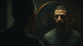 A dimly lit portrait of a man staring into a mirror, his reflection revealing a shadowed, contemplative expression, captures the essence of shadow work—facing the parts of ourselves we often ignore