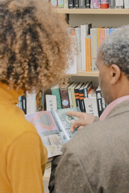 Duas pessoas folheam livro em biblioteca