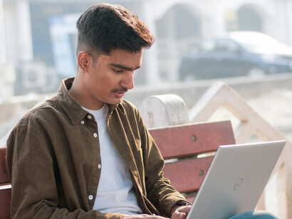A young Indian man sits in a park, searching for jobs on his laptop