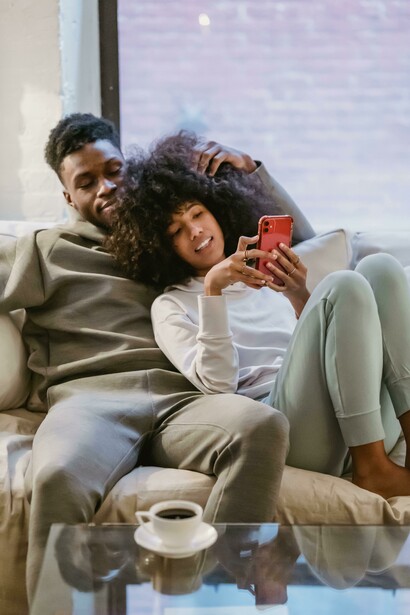 A joyful Black couple lounges on a couch, watching a vertical microdrama on a smartphone