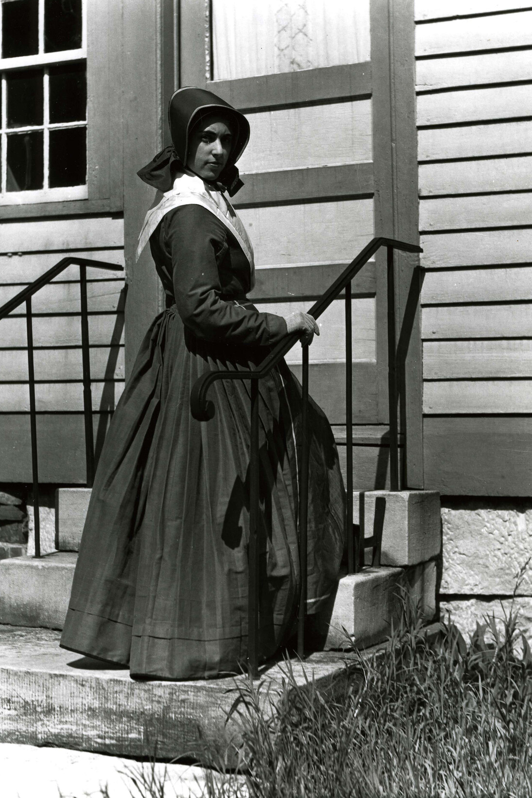 Model in Shaker weekday dress, on the steps of the Sisters’ Dairy and Weave Shop (Church Family, Hancock, Massachusetts)