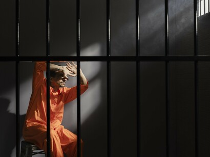 A man in a prison cell shields his eyes from a narrow shaft of light—symbolizing the millions denied bodily sovereignty in a system where immobility and dehumanization replace freedom