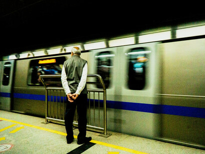 A man waits at a bustling subway station in India, observing the swift movement of the train, reflecting the overwhelming speed of societal transitions and the uncertainty of the times