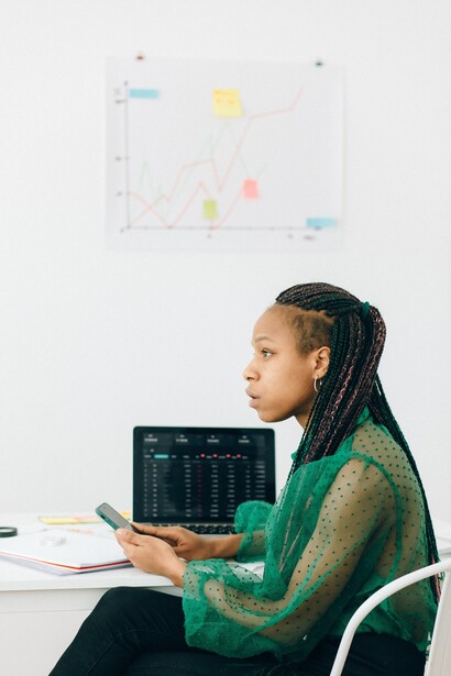 A woman sat at a desk using a laptop and a mobile phone