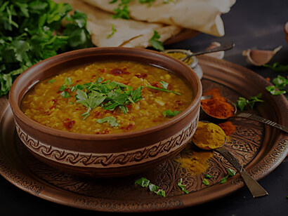 A steaming bowl of traditional Indian dal, a spicy lentil curry, is presented on a rustic black wooden background adorned with aromatic spices and herbs