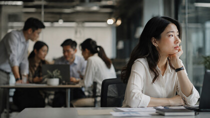 A woman sitting apart from her coworkers in a busy office, representing the emotional distance that can exist within a workplace