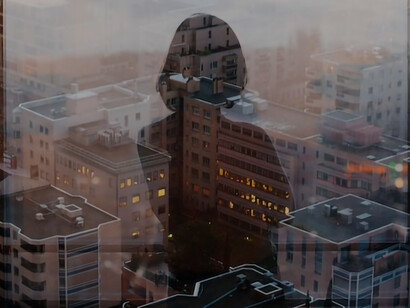 The reflection of a woman standing before a glass panel, gazing at high-rise and mid-rise buildings