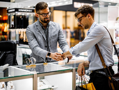 A watch seller attentively showing a wristwatch to a potential buyer at a retail kiosk