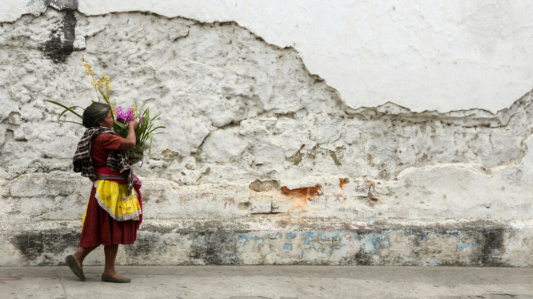 A woman carries a basket of flowers next to the cobblestone streets and crumbling walls of Antigua, Guatemala