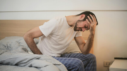 A man, getting up from bed, feeling exhausted