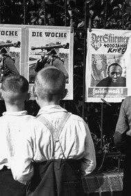 Niños alemanes leen propaganda nazi expuesta en una vía publica