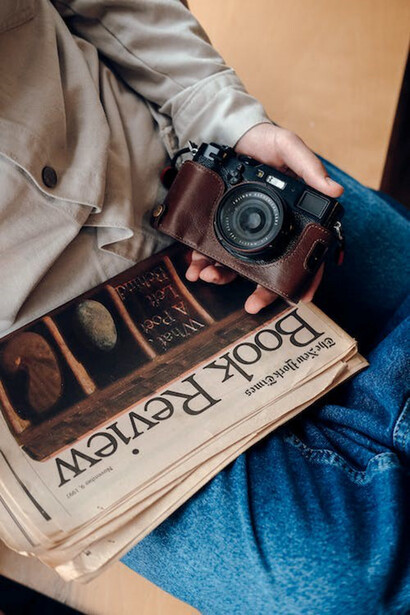 A man holding a retro analog camera and a newspaper