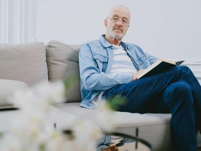 Homem relaxa lendo no sofá. Nessa nuvem de prazeres, o sol me chama, a praia clama, lembro da semana passada. Já saindo da praia recebo chamada ao vivo pelo WhatsApp
