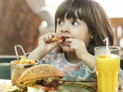 A little girl eats unhealthy fast food at a cafe, consuming ultra-processed junk food commonly marketed to kids