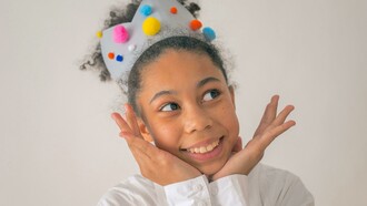 Menina negra feliz com coroa colorida com pompoms