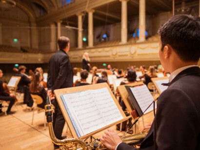 A man standing before a music stand with a music book inside the Culture Casino Bern, in Bern, Switzerland, as a saxophone plays during rehearsal