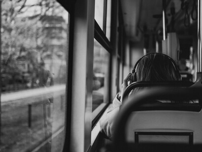 Black-and-white photo of a woman wearing headphones, sitting alone on a bus