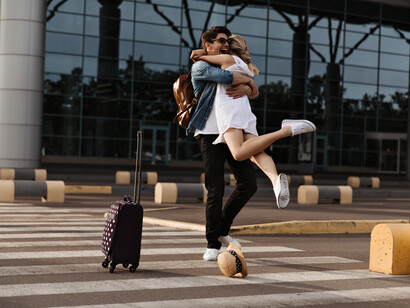 A joyful brunette man embraces his partner in a white dress during an emotional airport reunion after a long distance relationship