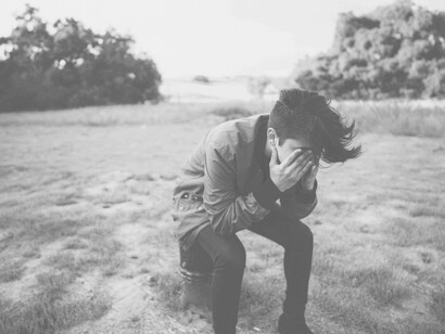 A man in a field with hands over his eyes as he tries to compose himself after receiving unwanted news