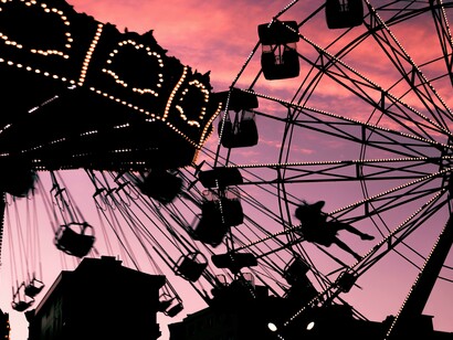 A photo of the silhouettes of a Ferris wheel and a carousel at dusk against a pink sky at the fair