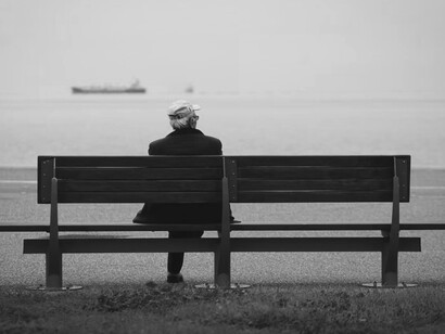 An older man sitting on a brown bench, looking out over the ocean