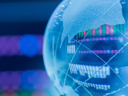 Mappamondo di vetro e grafici finanziari: "l’intento che sta alla base dei “finti dazi” e dei conseguenti dazi fintamente “reciproci” è quello di riportare la produzione, di aziende americane e di aziende straniere, all’interno del territorio degli Stati Uniti"