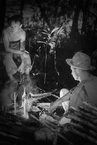 Perry Lowrey resting in front of a fire. Alejandro Laime in front of him. Photo by Ruth Robertson. Biblioteca Nacional de Venezuela Collection