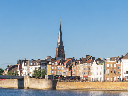 Maastricht, the Netherlands, a picturesque view of Maastricht’s riverside, featuring historic buildings, elegant church spires, and sunny summer weather