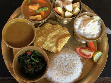 An assorted Newari meal from Nepal featuring bhat (rice), saag (leafy greens), dal (lentil soup), tarkari (vegetable curry), yogurt, papad, and fruit salad served together on a traditional plate