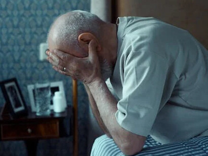 Elderly man sits distressed, head in hands, feeling the suffering of the human experience