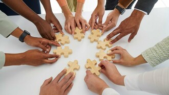 Mãos de diferentes pessoas movimentam peças de um quebra-cabeça sobre uma mesa. A construção coletiva de soluções está no centro da atuação do terceiro setor, que articula pessoas, recursos e competências em torno de objetivos sociais