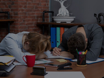 Young female and male co-workers feeling tired at office table, illustrating workplace exhaustion and the necessity for improvement in a challenging environment