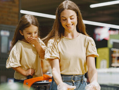People shopping at a supermarket, carefully reading labels and selecting groceries — a woman in a brown t-shirt stands out