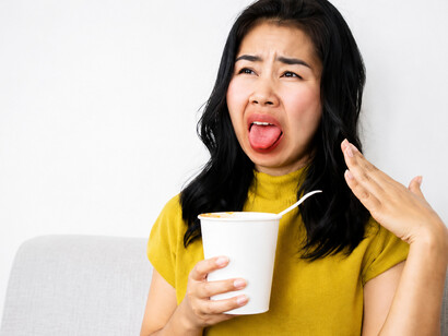 An Asian woman reacts to the intense heat of spicy cup noodles, fanning her mouth as her tongue burns from the fiery flavor