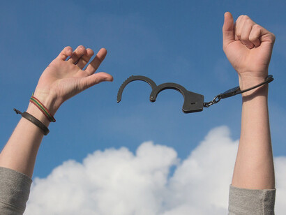 In the image, against the backdrop of the open sky, female hands are breaking free of handcuffs, symbolizing liberation, empowerment, and the triumph over adversity