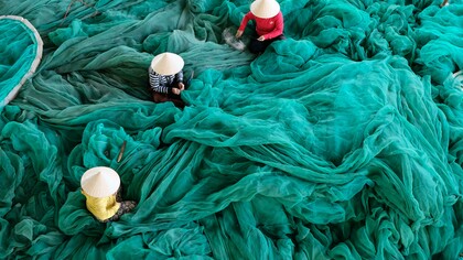Donne vietnamite che lavorano alla realizzazione di una grande rete verde
