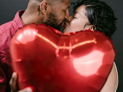 A couple kissing and showing their relationship intimacy while holding a heart balloon