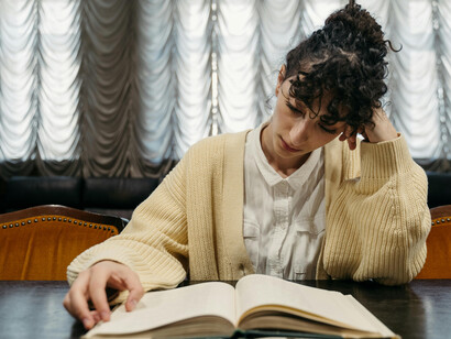 A woman in a knitted cardigan sits in the library, reading a book