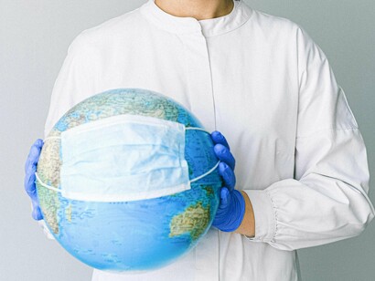 Mulher segura globo terrestre com máscara e luvas de proteção. Embora seja fundamental reconhecer os avanços que as vacinas proporcionaram no controle da pandemia, também é essencial que haja transparência na investigação de possíveis efeitos adversos