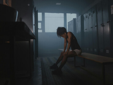 A woman alone in a dimly lit locker room, the empty space around her highlighting a sense of isolation and focus